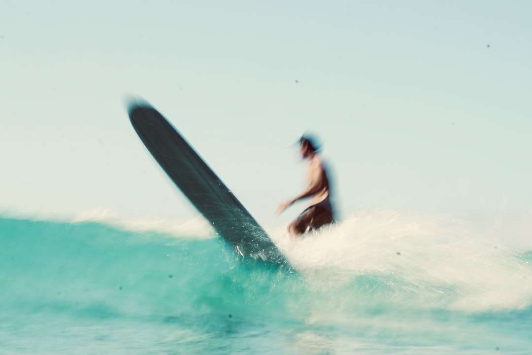昼間に海の波でサーフィンする黒いウェットスーツの男 ジグソーパズルオンライン