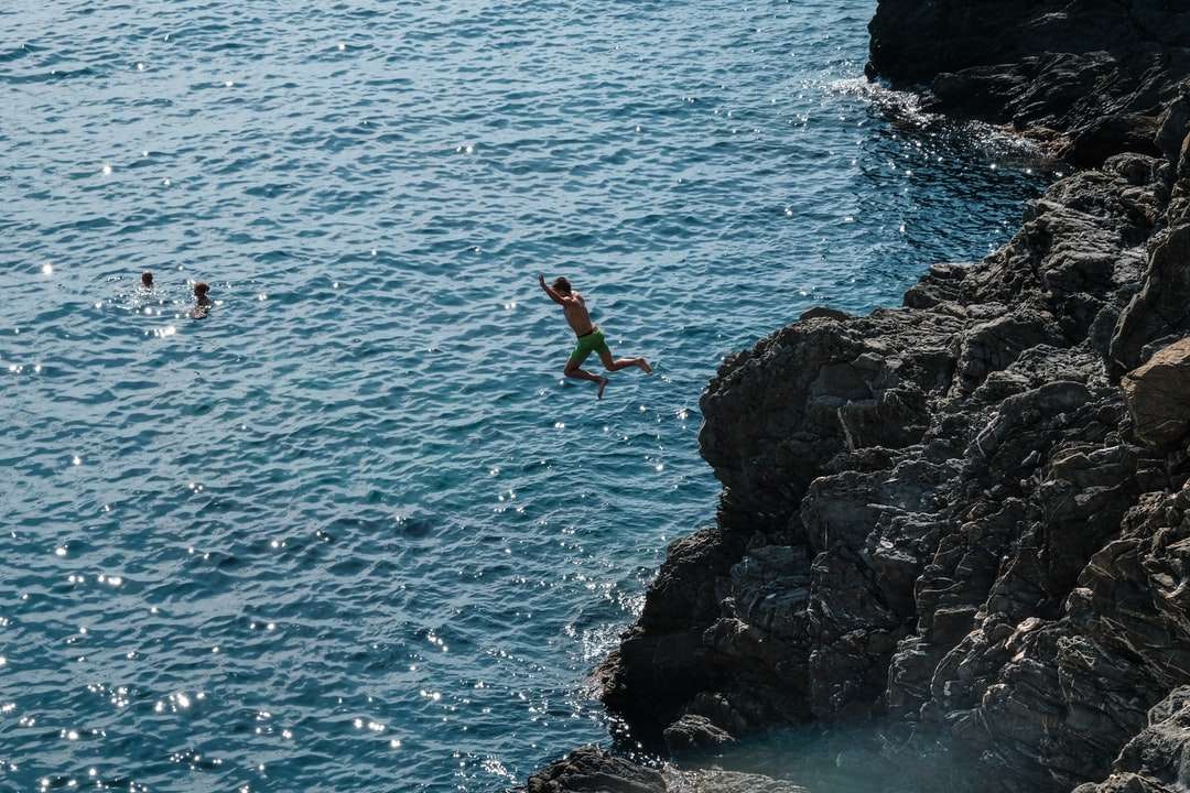 man in green shorts jumping on rocky cliff by the sea online puzzle