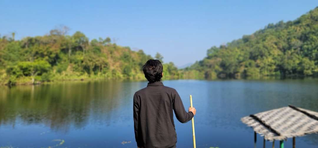 muž v šedé mikině drží žlutou hůl poblíž jezera online puzzle