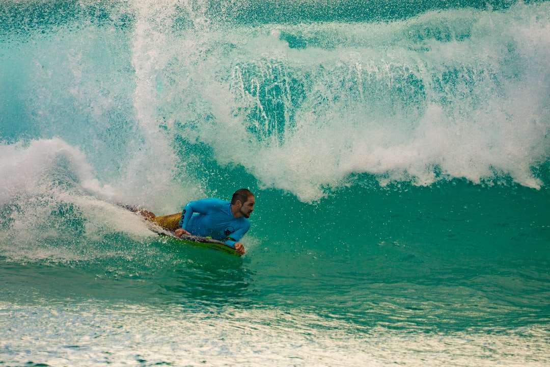 homme en chemise bleue surfant sur les vagues de la mer pendant la journée puzzle en ligne