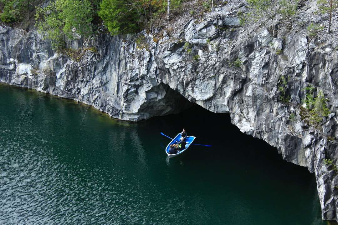 Mann im blauen Kajak auf Fluss nahe grauem felsigem Berg Online-Puzzle