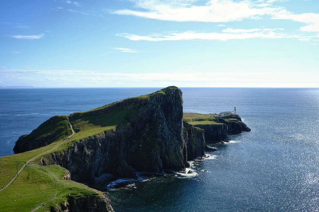 zöld és fekete sziklaalakzat a tenger mellett, kék ég alatt kirakós online