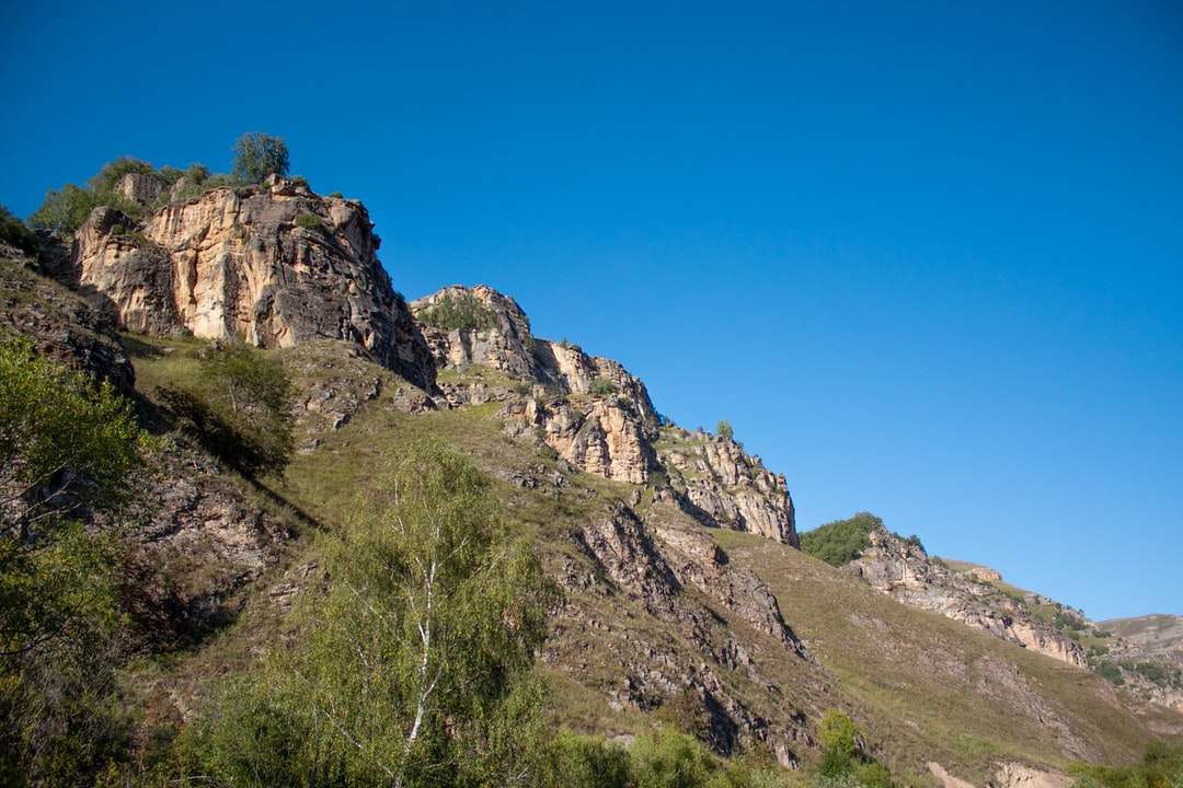 groen gras op rotsachtige berg onder blauwe hemel overdag online puzzel