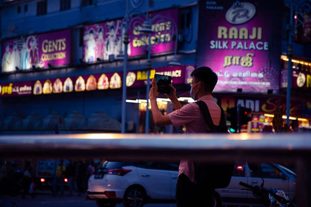άντρας σε λευκό μπλουζάκι λήψη φωτογραφίας του καταστήματος κατά τη διάρκεια της νύχτας παζλ online