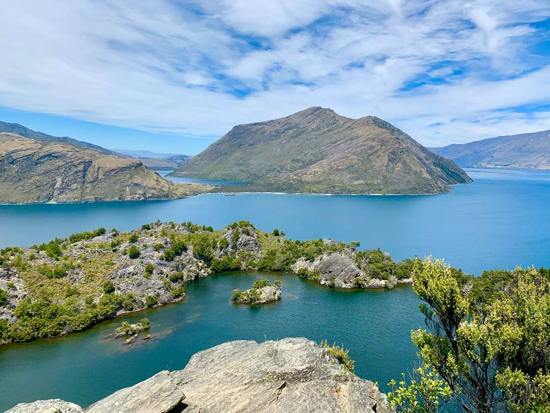 montagna verde e marrone accanto al lago sotto il cielo blu puzzle online