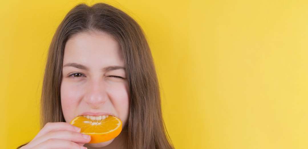 κοπέλα που κρατά πορτοκαλί φρούτα μπροστά από τον κίτρινο τοίχο παζλ online