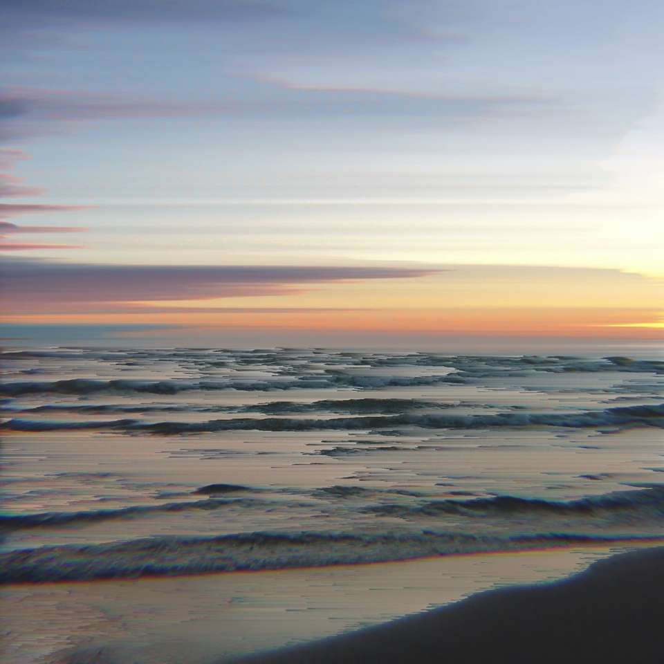 havsvågor som kraschar på stranden under solnedgången Pussel online
