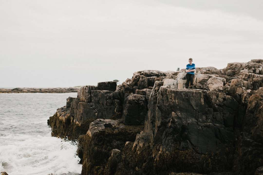 Mann im blauen Hemd sitzt auf Felsformation nahe Körper Puzzlespiel online