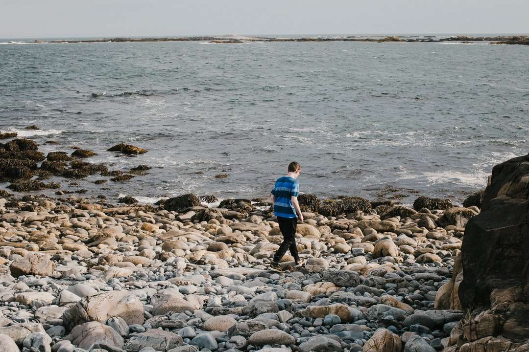 岩の多い海岸を歩く青いシャツと黒のズボンの少年 ジグソーパズルオンライン
