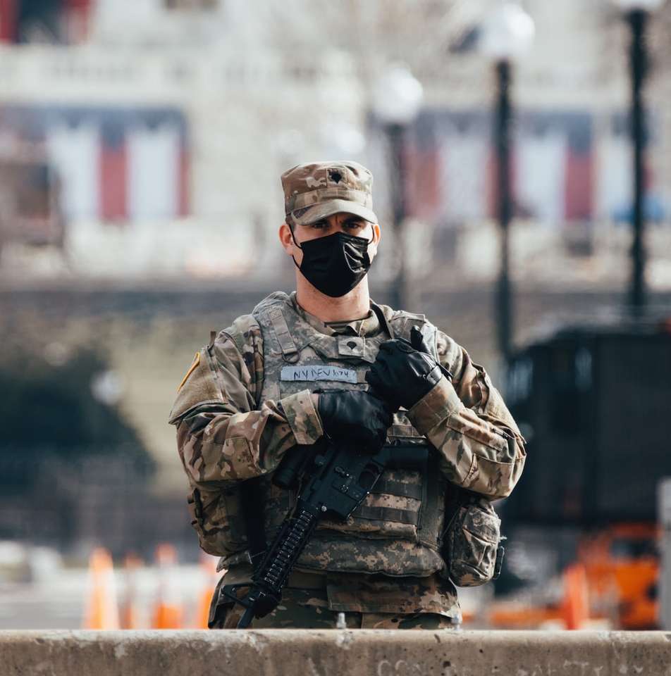 Hombre en uniforme de camuflaje negro y marrón sosteniendo un rifle rompecabezas en línea
