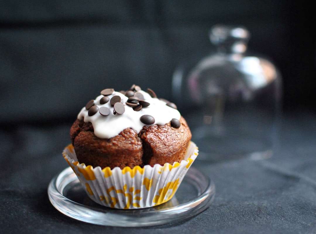 Schokoladencupcake mit weißem Zuckerguss auf klarer Glasuntertasse Online-Puzzle