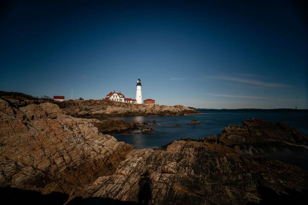 white lighthouse on brown rock formation near body of water jigsaw puzzle online