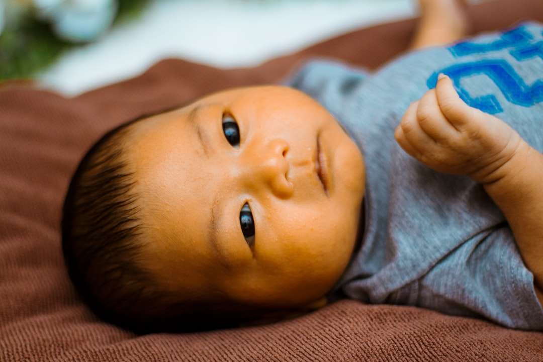 bebis i grå skjorta som ligger på brun textil pussel på nätet