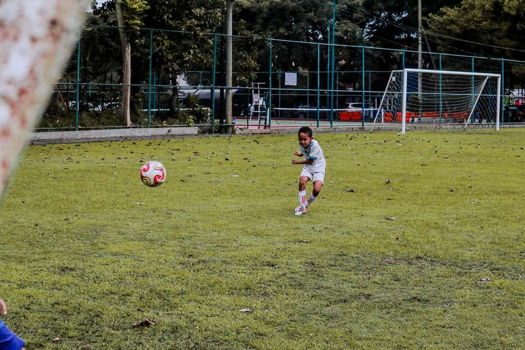 2 băieți care joacă fotbal pe teren cu iarbă verde în timpul zilei jigsaw puzzle online