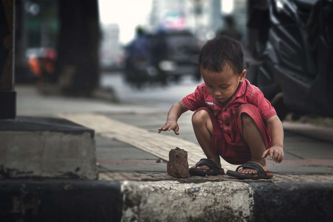 Niño en camiseta roja con cuello redondo sentado sobre pavimento de hormigón rompecabezas en línea
