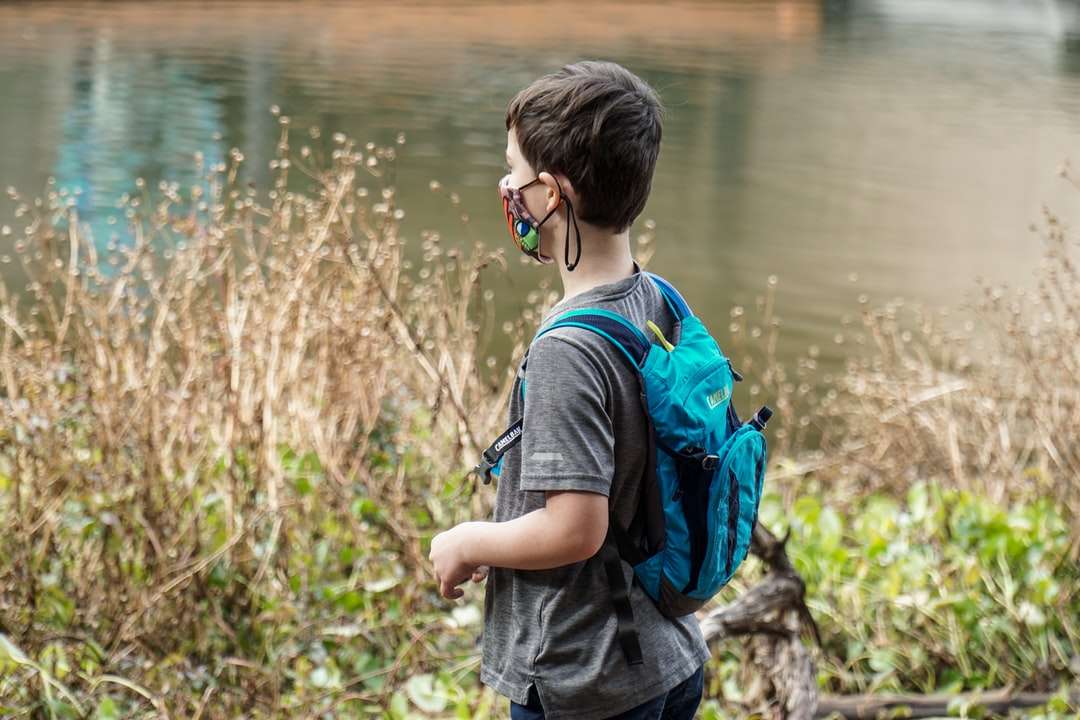 chlapec v modrém a černém batohu stojící poblíž vodní plochy online puzzle