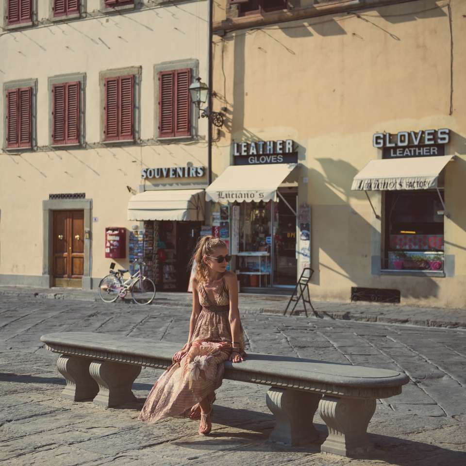 жена в кафява рокля, седнала на пейка близо до сградата онлайн пъзел