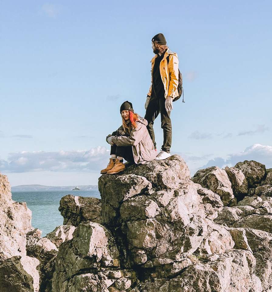 Paar sitzt auf Felsformation in der Nähe von Gewässern Puzzlespiel online