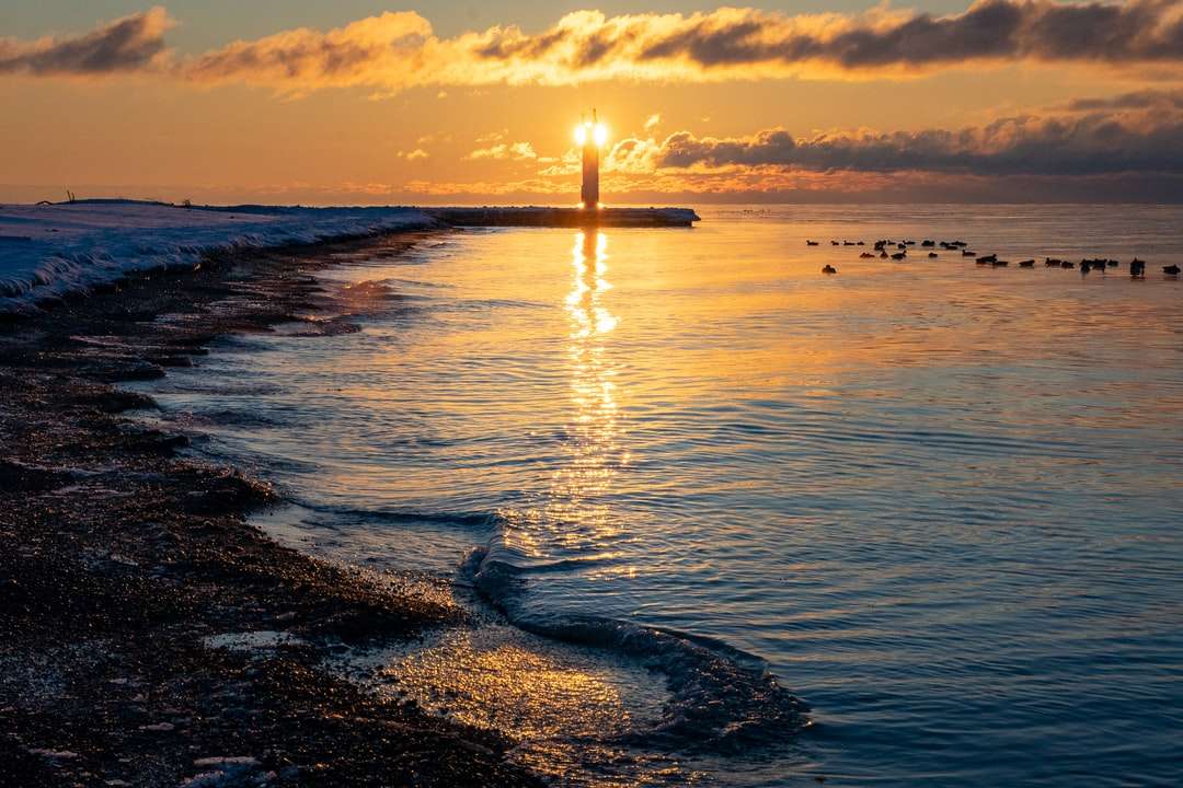 Silhouette des Leuchtturms am Strand während des Sonnenuntergangs Online-Puzzle