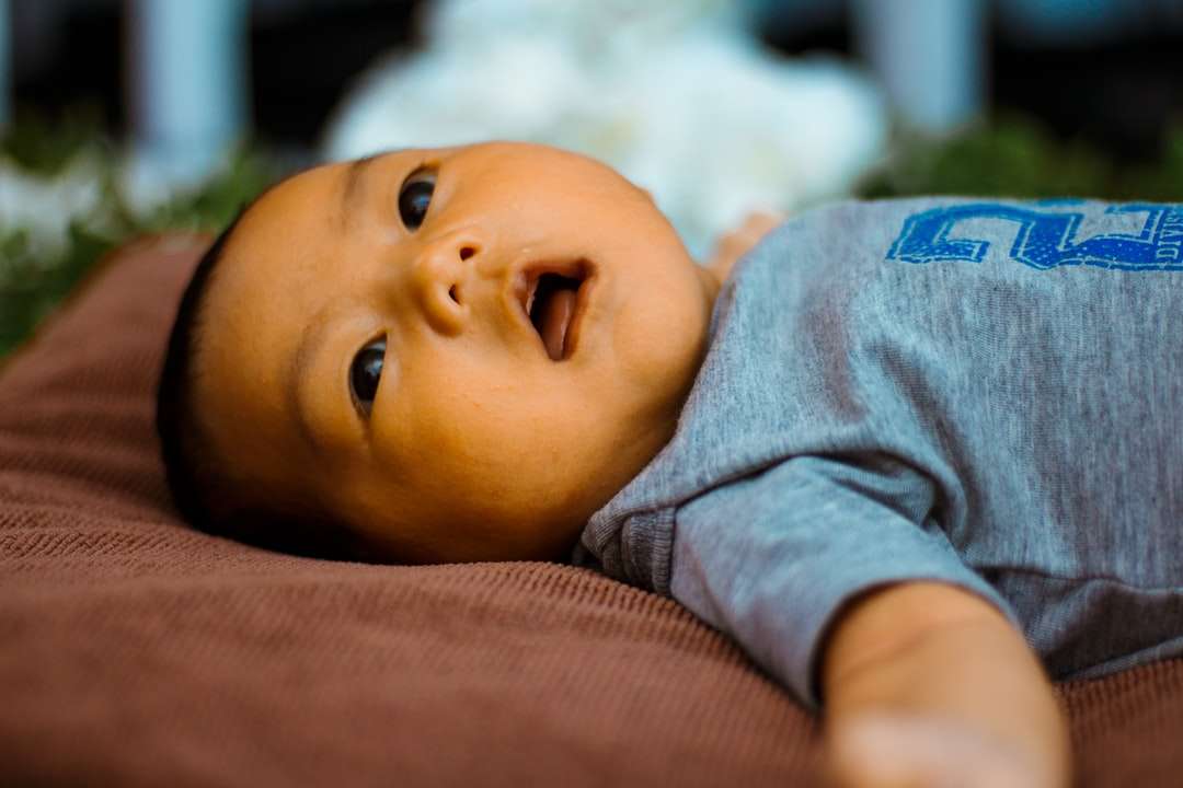 Baby im grauen Hemd, das auf braunem Textil liegt Online-Puzzle