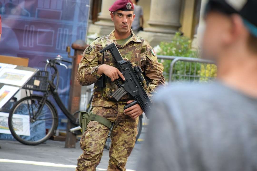Hombre en uniforme de camuflaje verde y marrón sosteniendo un rifle rompecabezas en línea
