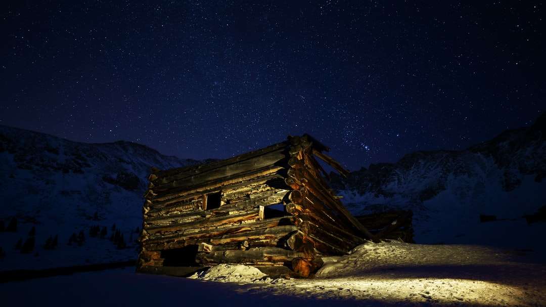 braunes Holzhaus auf schneebedecktem Boden während der Nachtzeit Puzzlespiel online