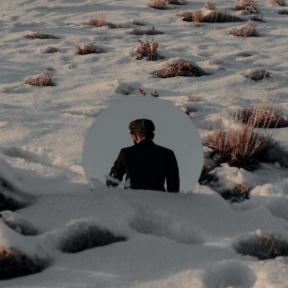 Person im schwarzen Mantel sitzt auf schneebedecktem Boden Online-Puzzle