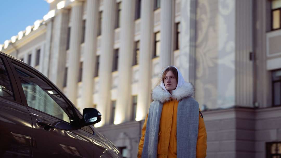 жінка в коричнево-білому халаті стоїть біля чорного автомобіля пазл онлайн