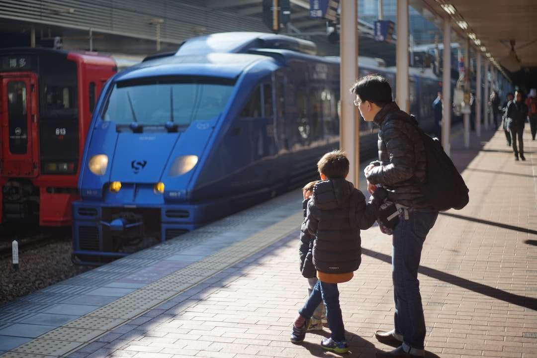 man in black jacket standing beside blue train online puzzle