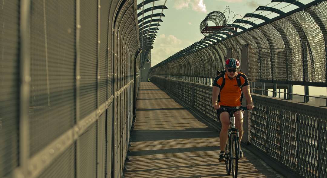 мужчина в оранжевой рубашке едет на велосипеде по мосту в дневное время пазл онлайн