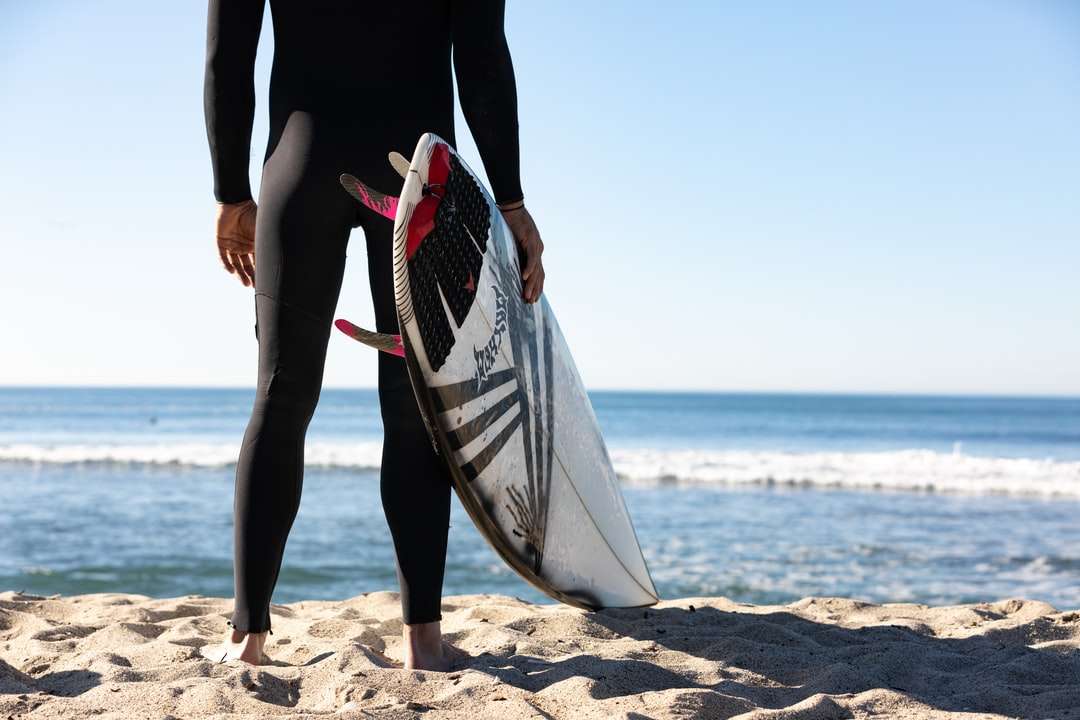 person som håller vit och blå surfbräda som står på stranden Pussel online