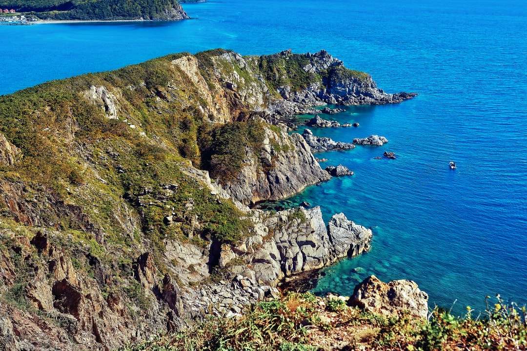 Formación rocosa verde y marrón junto al mar azul rompecabezas en línea