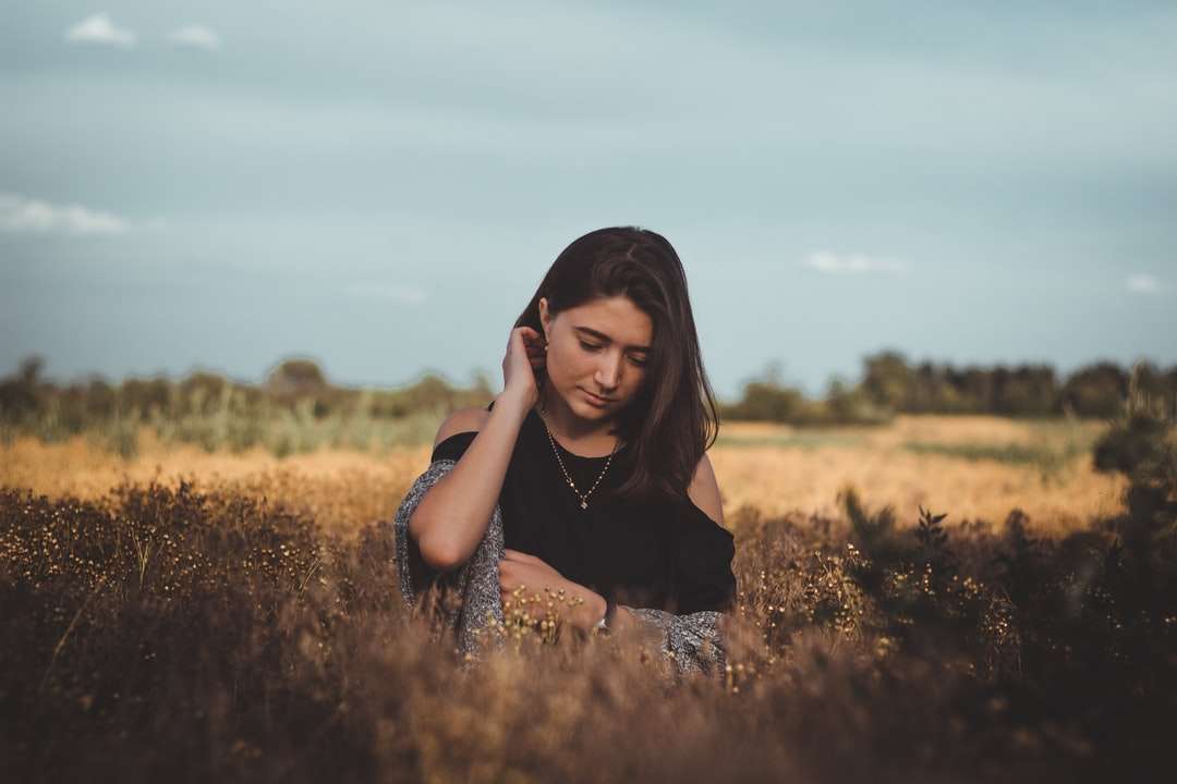 женщина в черной рубашке сидит на поле с коричневой травой онлайн-пазл