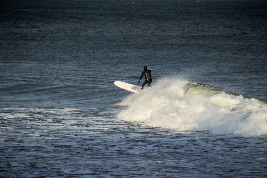 uomo in muta nera che guida la tavola da surf bianca sulle onde del mare puzzle online
