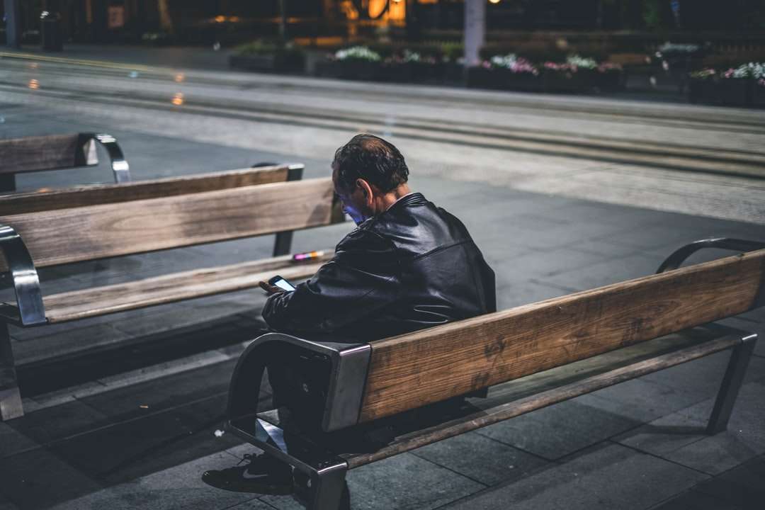 Mann in schwarzer Jacke sitzt auf brauner Holzbank Online-Puzzle