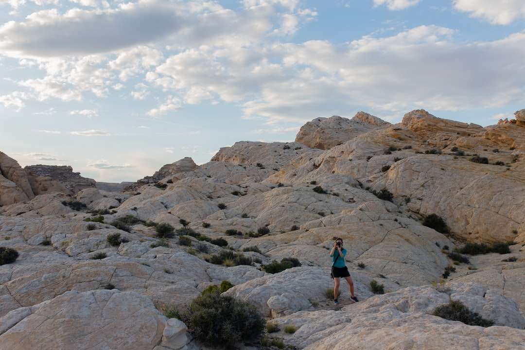 Persona en chaqueta azul de pie sobre la colina rocosa durante el día rompecabezas en línea