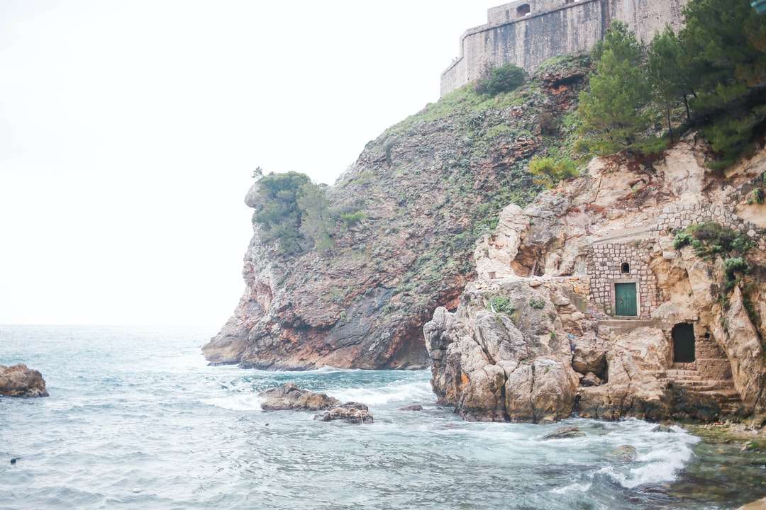 Edificio de hormigón marrón sobre un acantilado junto al mar durante el día rompecabezas en línea