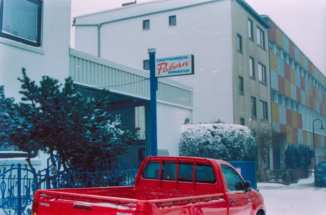 röd lastbil för besättningshytt parkerad nära vit byggnad Pussel online