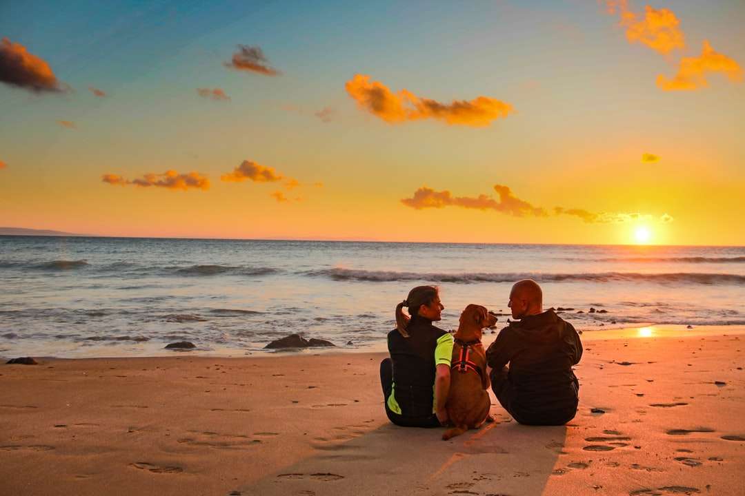 man and woman sitting on beach during sunset online puzzle