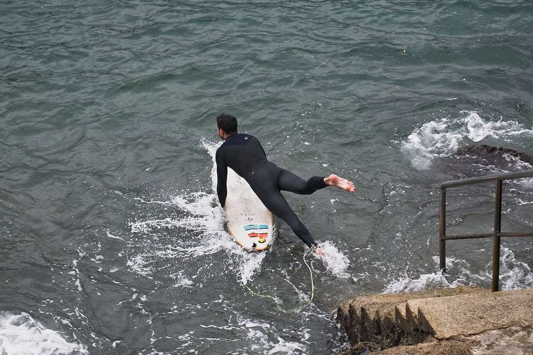 homem de terno preto segurando uma prancha de surf amarela e vermelha puzzle online