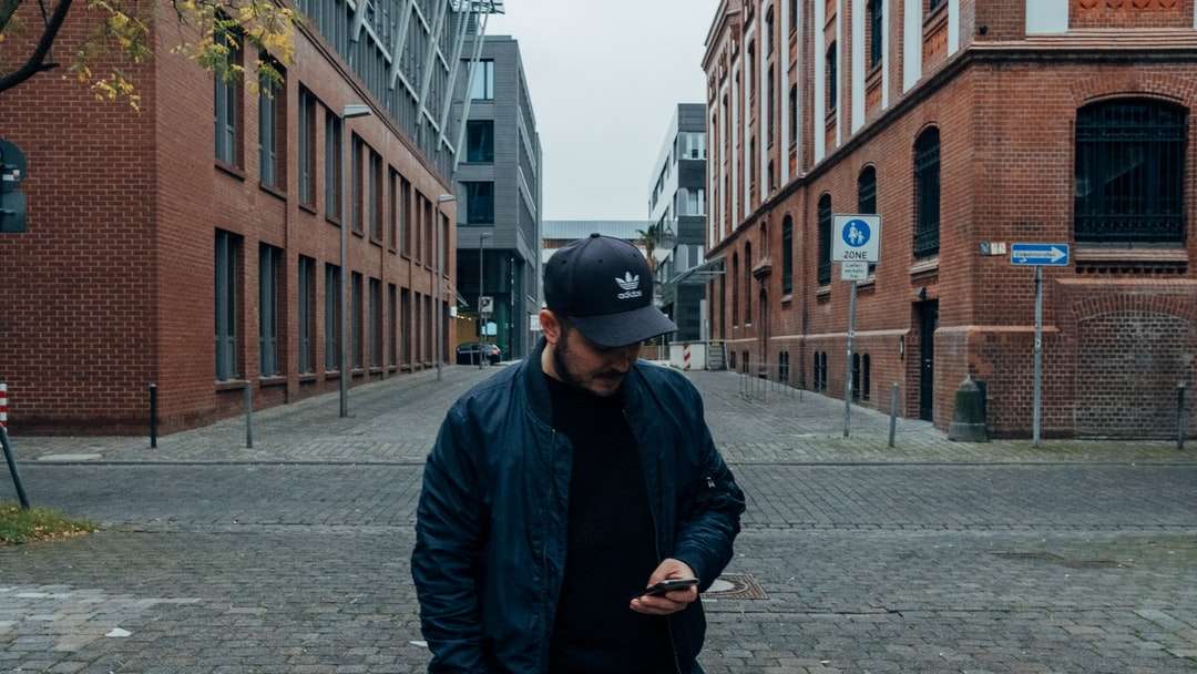 мужчина в черной куртке и черной кепке стоит на тротуаре онлайн-пазл