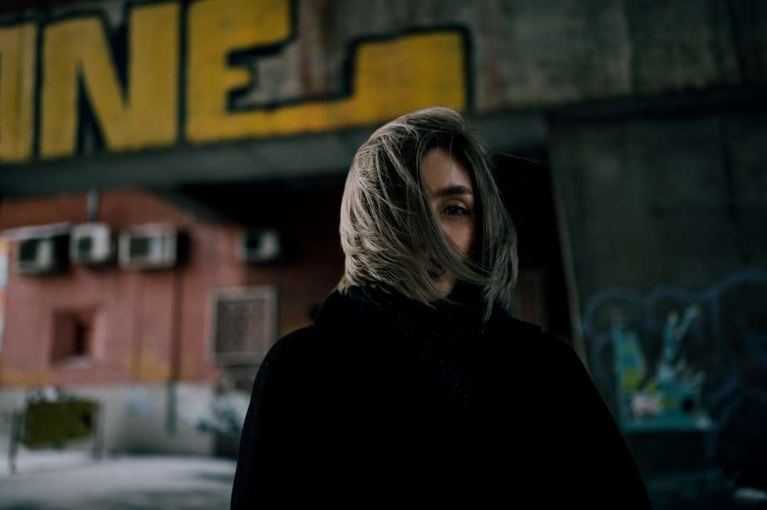 жінка в чорному пальті стоїть біля коричневої будівлі онлайн пазл