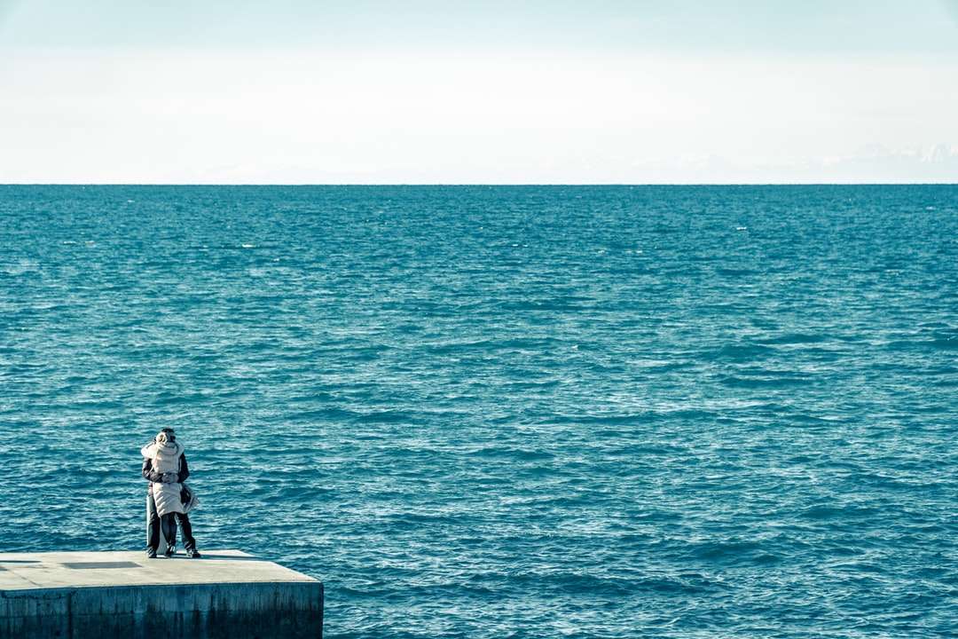 Hombre de chaqueta negra sentado en un banco de hormigón cerca del mar rompecabezas en línea