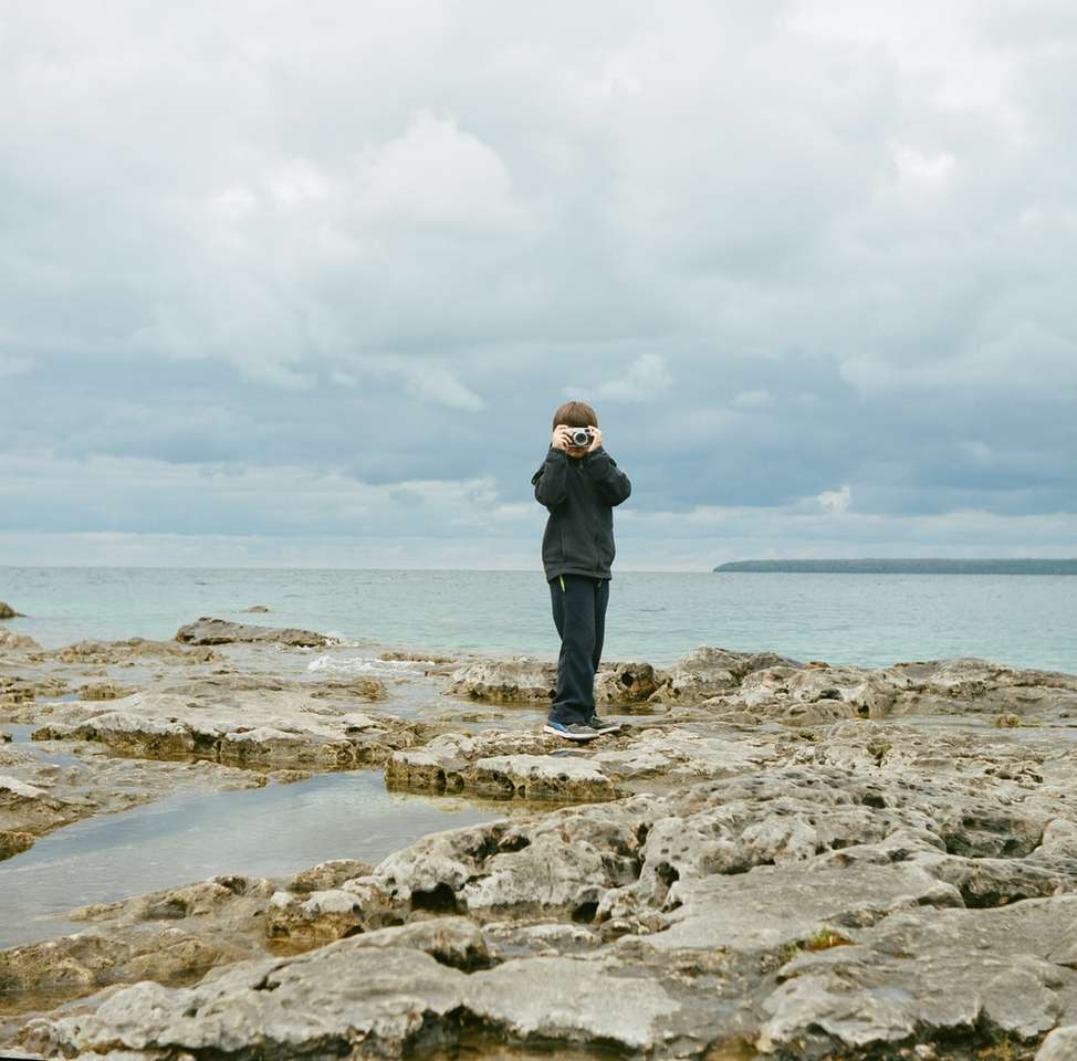 uomo in piedi sulla formazione rocciosa vicino al corpo idrico puzzle online