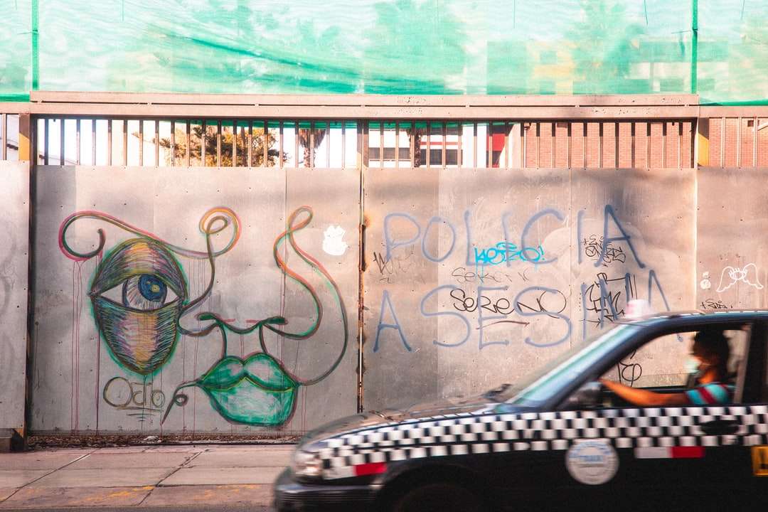 Coche negro aparcado junto a la pared blanca y azul con graffiti rompecabezas en línea