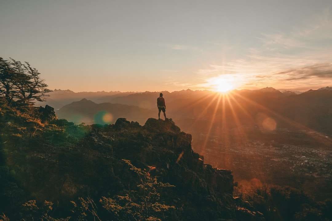 silueta de persona de pie sobre una roca durante la puesta de sol rompecabezas en línea