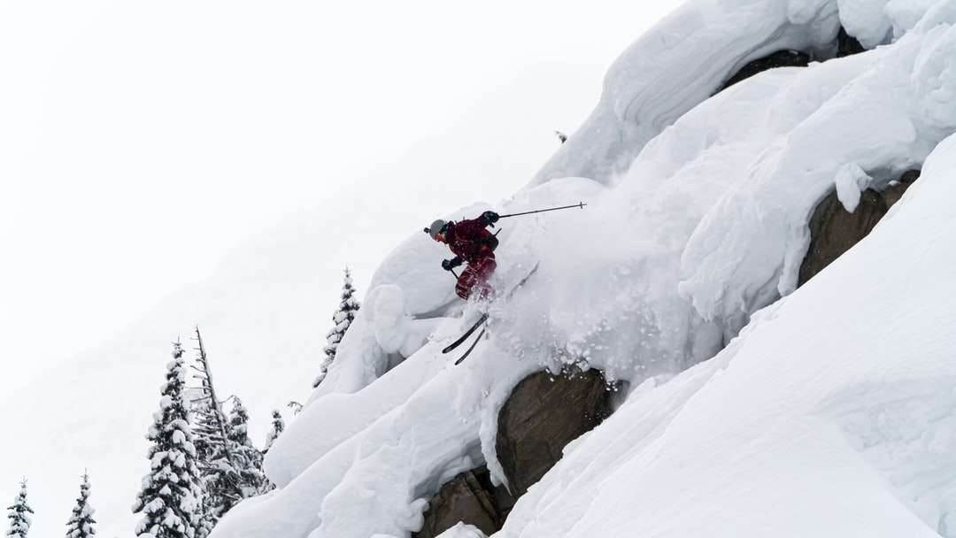 Persona con chaqueta roja y pantalón negro montando cuchillas de esquí. rompecabezas en línea