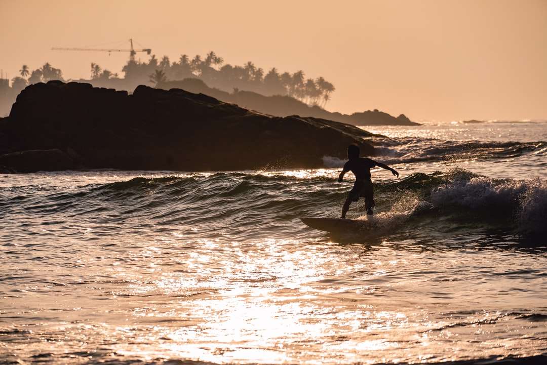 silueta de persona surfeando en el mar durante la puesta de sol rompecabezas en línea