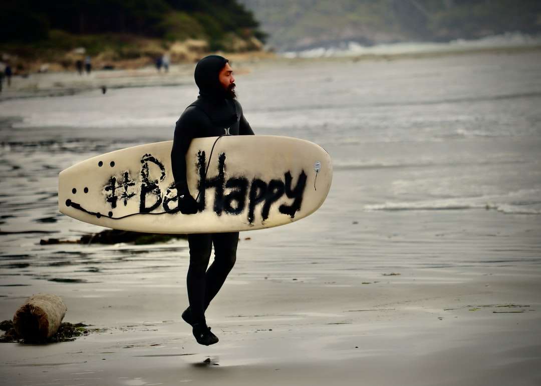 Homme en sweat à capuche noir portant une planche de surf blanche puzzle en ligne