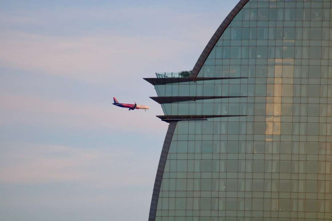 rotes und weißes Flugzeug, das über Glasgebäude fliegt Puzzlespiel online
